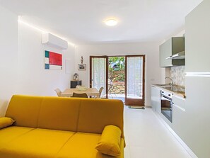 Ein modernes Wohnzimmer mit einer Couch, einem Essbereich mit Tisch und Stühlen, einer Küche mit Herd und Schränken sowie einer Glastür, die zu einem Außenbereich führt.
