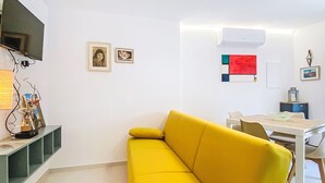 A bright yellow sofa in a modern living area with a flat-screen TV, artwork on the walls, and a dining table with chairs. - La Tana by Interhome (Castiglioncello)
