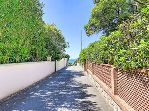 A narrow street flanked by dense greenery and a clear blue sky. - La Tana by Interhome (Castiglioncello)
