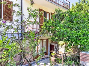 A two-story building with balconies, a stone wall, and a small garden area with plants and flowers. - La Tana by Interhome (Castiglioncello)