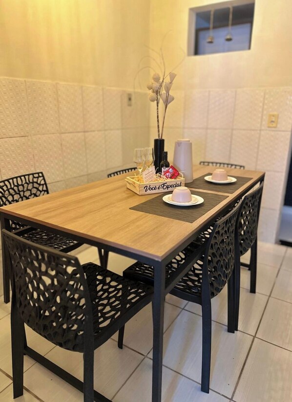 Uma mesa de jantar com cadeiras pretas, uma mesa de madeira e um tabuleiro com uma garrafa e copos.