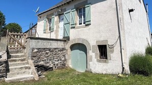Ein zweistöckiges Steinhaus mit einer Steintreppe, einer grünen Tür und einer Satellitenschüssel.
