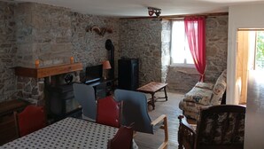 Ein rustikaler Raum mit Steinwänden, einem Kamin, einem Fernseher, einem Esstisch und einem Sofa.