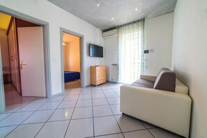 Ein modernes Wohnzimmer mit einer Couch, einem an der Wand montierten Fernseher und einem Fenster mit Vorhängen.