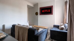 Una sala de estar con un sofá, un sillón, una mesa de centro y un televisor de pared que muestra 'NETFLIX'.