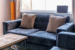 A dark blue sofa with two woven pillows, a wooden coffee table, and a laptop on a windowsill. - Inviting 3BR Norton Home Sleeps 7 by Stay With Us (Norton)