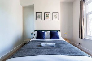 A neatly made bed with a blue and white patterned bedspread, two dark blue pillows, and a folded white towel. There are three framed botanical prints on the wall above the bed. - Inviting 3BR Norton Home Sleeps 7 by Stay With Us (Norton)