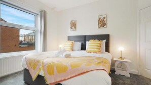 Une chambre à coucher avec un lit, une fenêtre, une table de chevet avec une lampe et des œuvres d’art accrochées au mur.