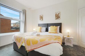 Ein Schlafzimmer mit Bett, Fenster, Nachttisch mit Lampe und einem Bild an der Wand.