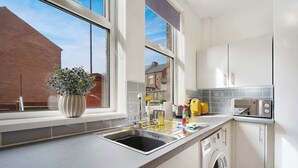 Une cuisine moderne dotée d’un lave-linge encastré, d’une grande fenêtre et offrant une vue sur un immeuble en briques.