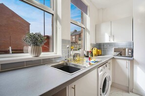 Eine moderne Küche mit eingebauter Waschmaschine, einem großen Fenster und Blick auf ein Backsteingebäude.