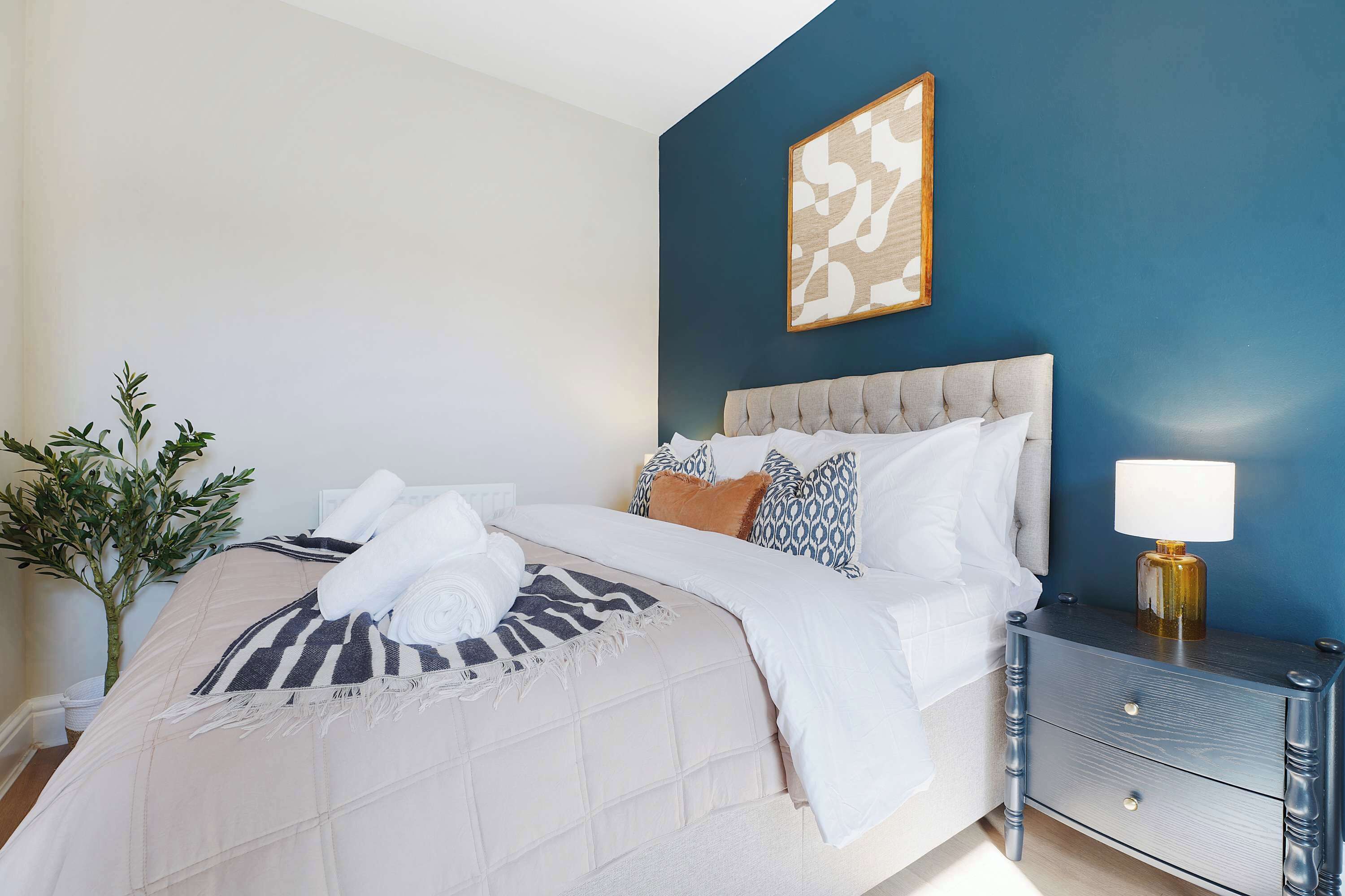 A neatly made bed with a striped blanket, a bedside lamp, and a nightstand with drawers.