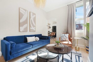 Ein Wohnzimmer mit einem blauen Sofa, einem runden Glastisch und abstrakter Wandkunst.