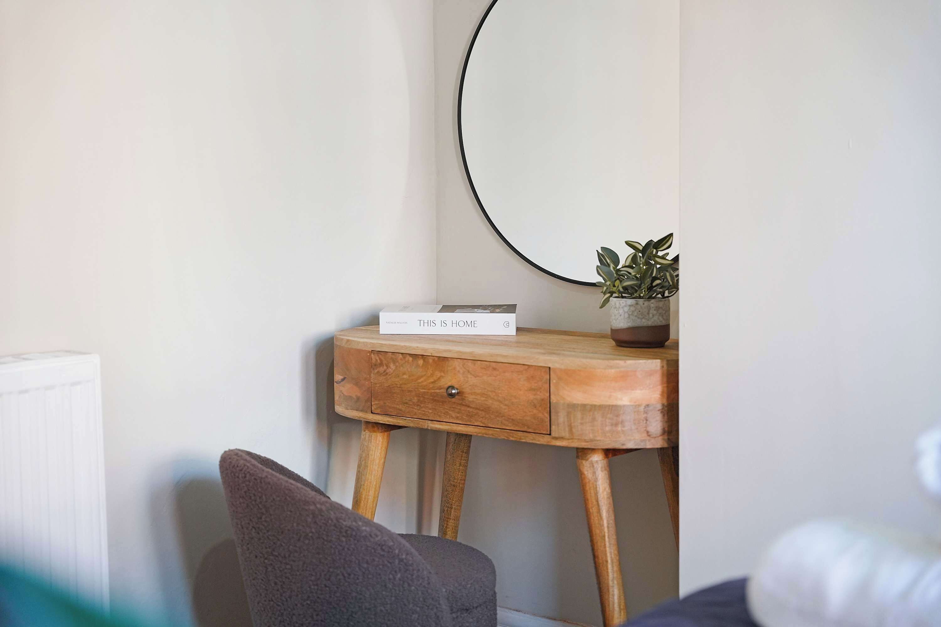Une chambre avec une table de chevet en bois, un miroir, une petite plante en pot et une pancarte sur laquelle on peut lire : « ICI, C’EST CHEZ MOI ».