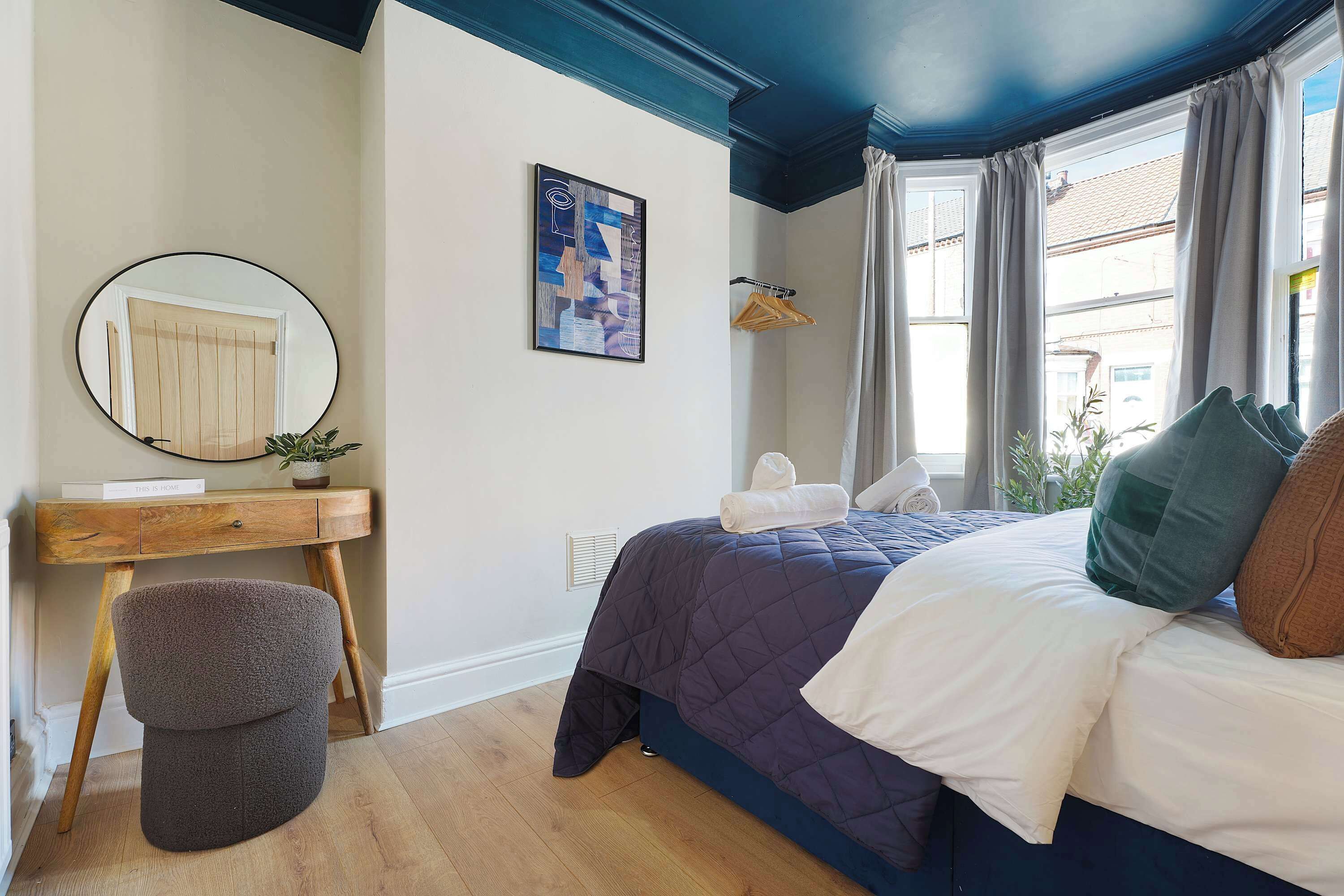 Une chambre à coucher avec un lit, un bureau, une chaise, un miroir et une fenêtre avec des rideaux.