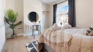Une chambre à coucher avec un lit, un bureau, une chaise, une plante en pot, un miroir et une fenêtre avec des rideaux.