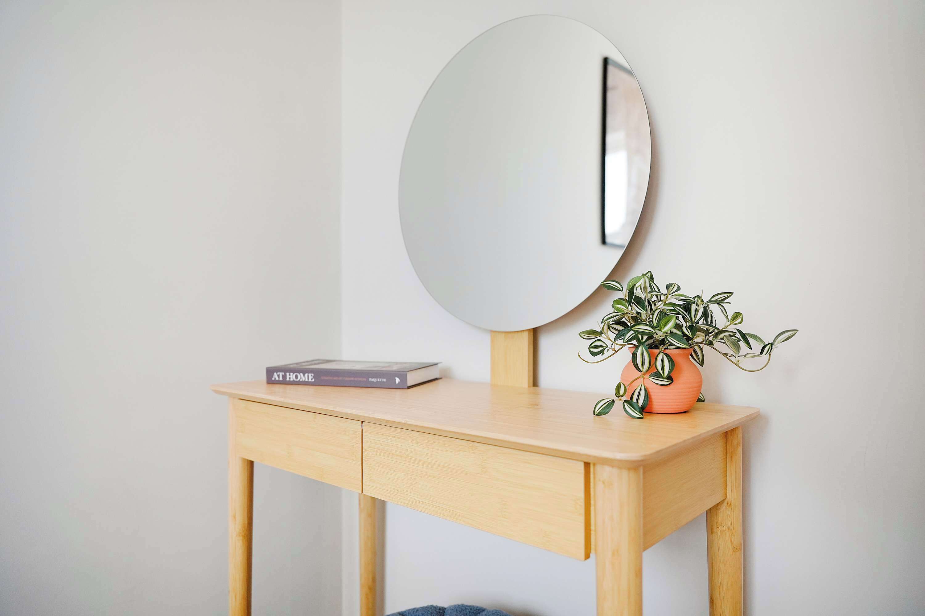 A wooden desk with a round mirror, a book, and a potted plant.
