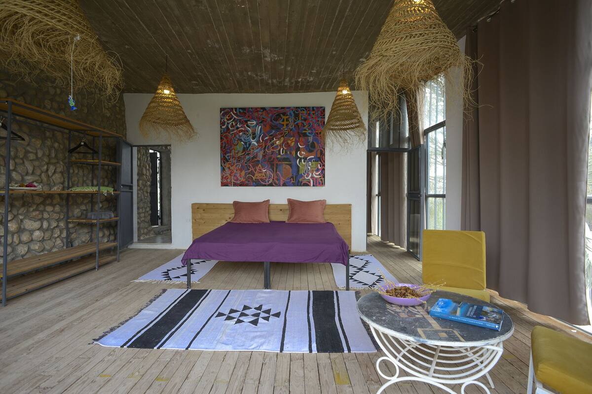 Un dormitorio con cama, un cuadro, una ventana y una mesa con un tazón y un libro.