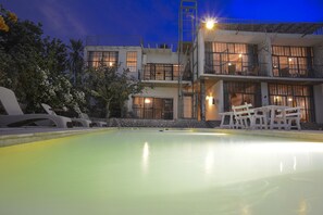 A pool with lounge chairs, a building with multiple balconies, and a staircase leading to the upper levels.