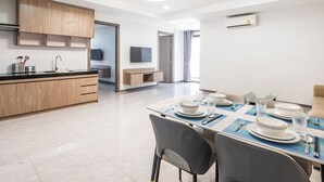 A modern kitchen with wooden cabinets, a dining area with a table set for four, and a TV mounted on the wall. - H Resident (Phnom Penh)