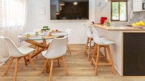 Une cuisine moderne avec un coin repas, un plancher en bois, des chaises blanches et un grand téléviseur.