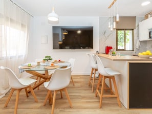 Eine moderne Küche mit Essbereich, Holzboden, weißen Stühlen und einem großen Fernseher.