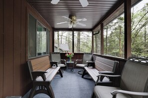 En overdækket veranda med træbænke, et bord og en loftsvifte.