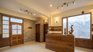 A reception area with a wooden reception desk, stone walls, and large windows with a mountain view. - Biker Gang Hotel & Cafe By OTABoostup (Keylong)