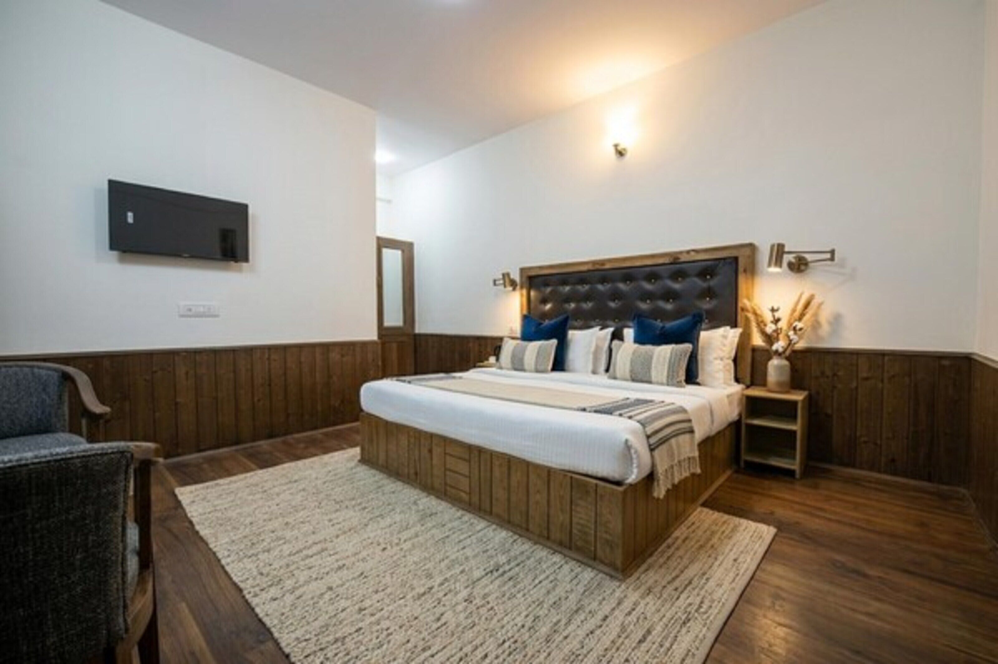 Ein Schlafzimmer mit einem Holz-Kopfteil, einem an der Wand montierten Flachbildfernseher, einem Nachttisch mit Lampe und einem Sessel.