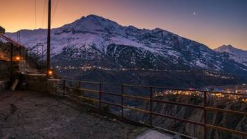 A mountainous landscape with a snow-covered peak, a distant town, and a metal railing.