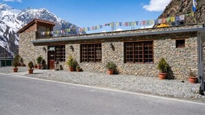 A stone building with a balcony, windows, and potted plants. - Biker Gang Hotel & Cafe By OTABoostup (Keylong)