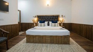 A bedroom with a wooden headboard, a bed with white bedding, two bedside lamps, and a wall-mounted TV. - Biker Gang Hotel & Cafe By OTABoostup (Keylong)