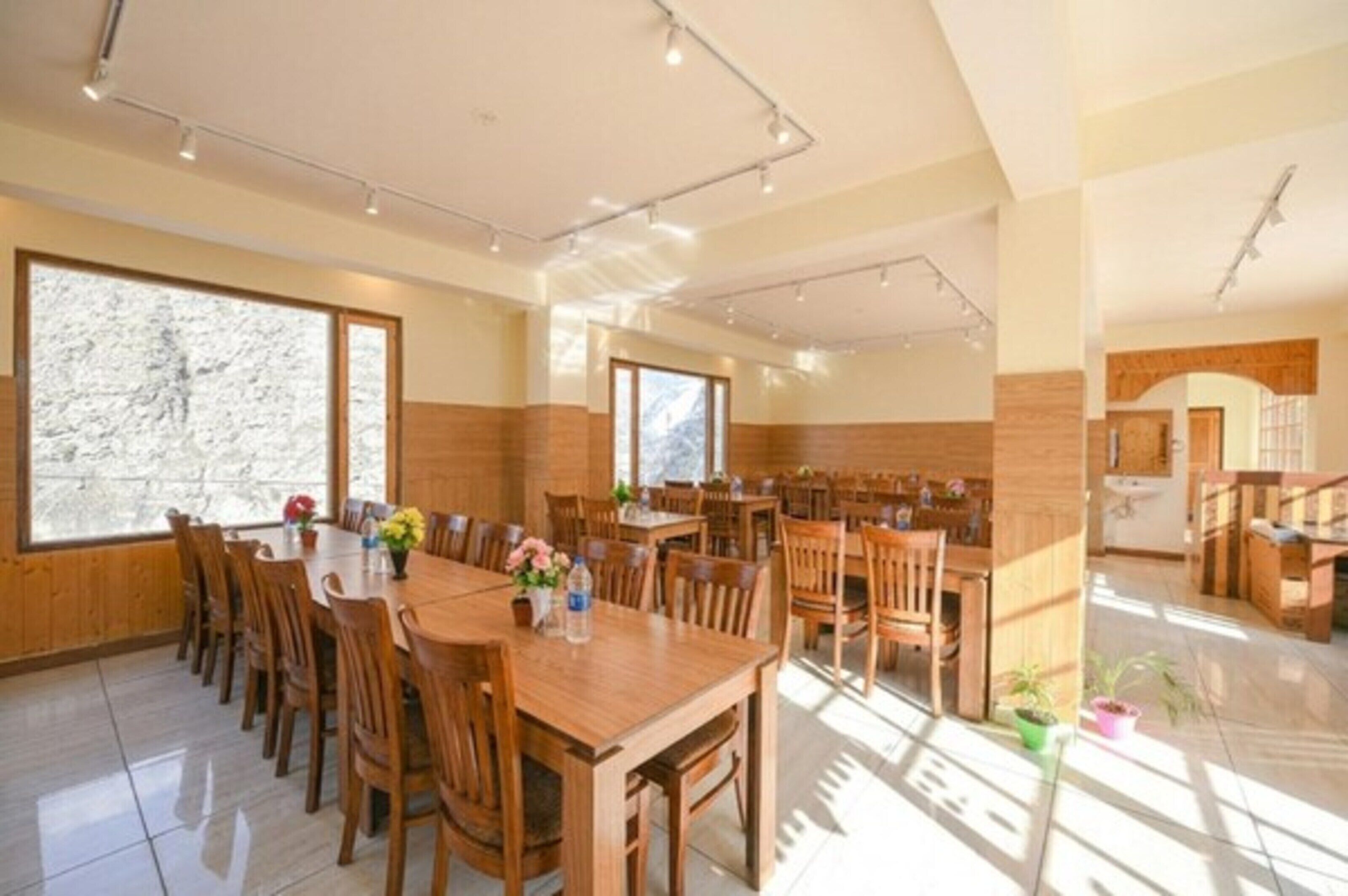 Un comedor amplio con mesas y sillas de madera, ventanas grandes y una cocina visible al fondo.