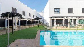 Ein moderner Poolbereich mit klarem, blauem Pool, umgeben von einer Holzterrasse und künstlichem Rasen.