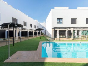 Ein moderner Poolbereich mit klarem, blauem Pool, umgeben von einer Holzterrasse und künstlichem Rasen.