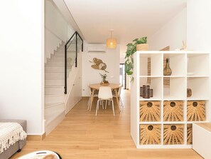 Un interior moderno con una escalera, zona de comedor y una estantería blanca con cestas tejidas.