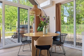 A modern dining area with a round wooden table, black chairs, a woven pendant light, and a vase with flowers. - A cosy bungalow for four people with its own hot tub, situated in the green heart of Drenthe amongst the woods of Gasselte (Gasselte)