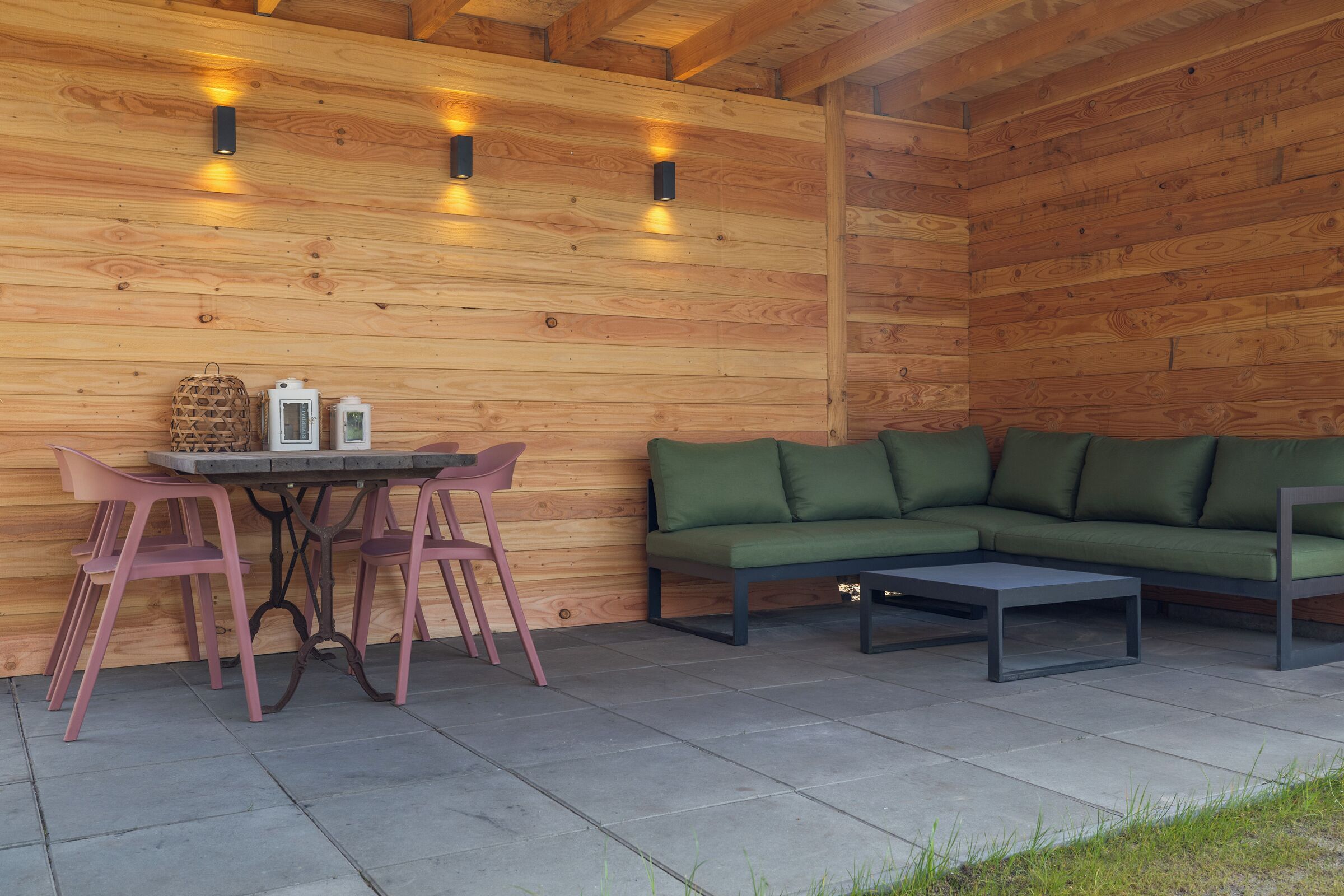 A wooden cabin interior with a table, chairs, a sofa, and wall-mounted lights.
