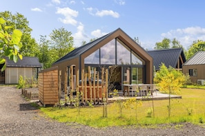 A modern house with a large glass window, a wooden deck, and a small shed. - A cosy bungalow for four people with its own hot tub, situated in the green heart of Drenthe amongst the woods of Gasselte (Gasselte)