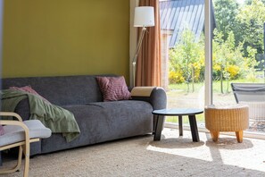 A modern living room with a sofa, a small round table, a wicker stool, and a floor lamp.