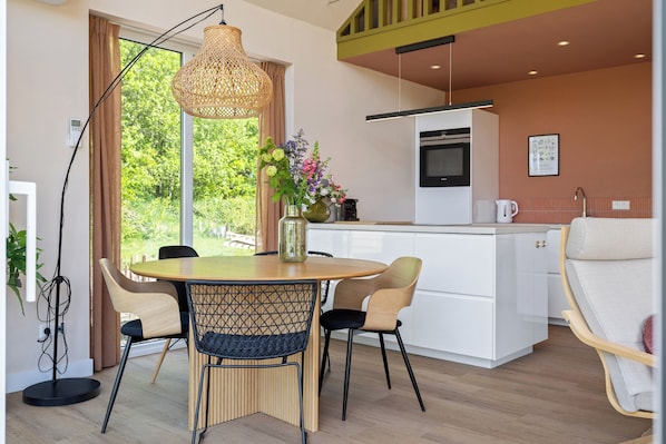 A modern kitchen with white cabinets, a dining area with a round table and chairs, and a large window with a view of greenery.