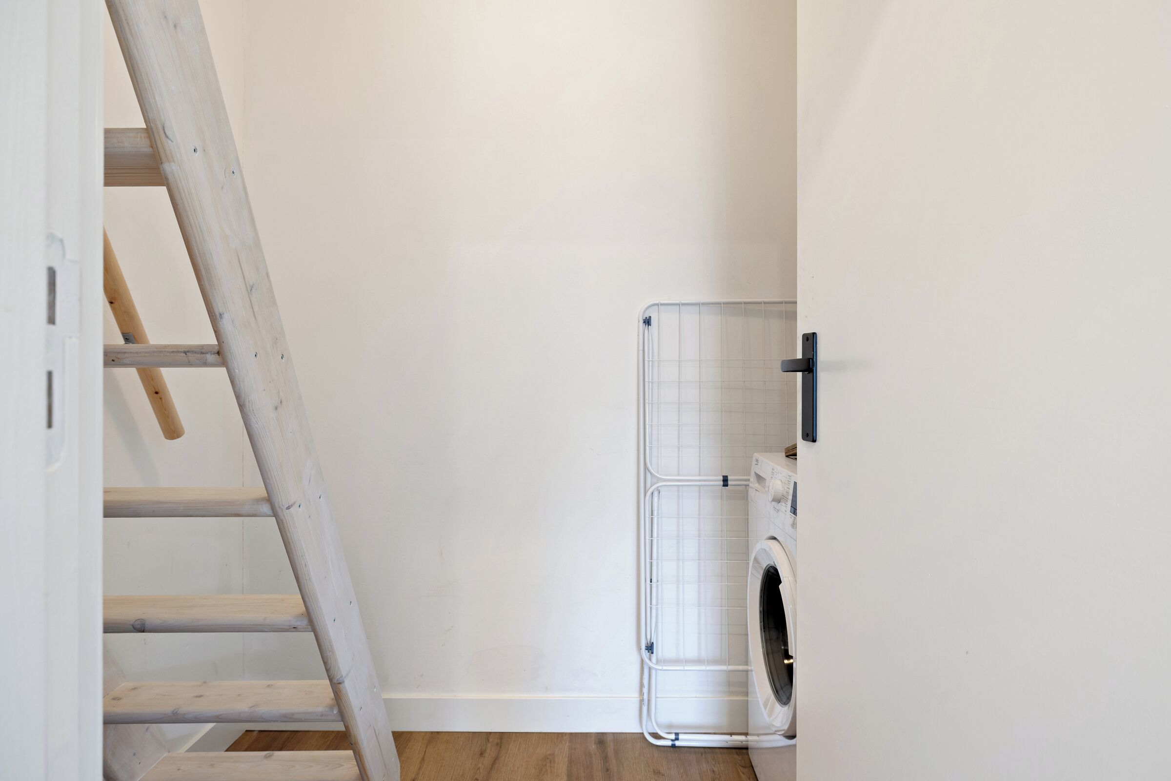 A laundry area with a washing machine, a drying rack, and a wooden ladder.