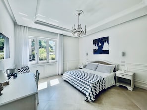 Ein Schlafzimmer mit Bett, Nachttischen, einer Chandelieber, einem Fenster mit Vorhängen und einem Wandbild.