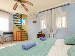 Ein Schlafzimmer mit Wendeltreppe, einem Bett mit grün-weißer Bettwäsche, einem Stuhl und einem Deckenventilator.
