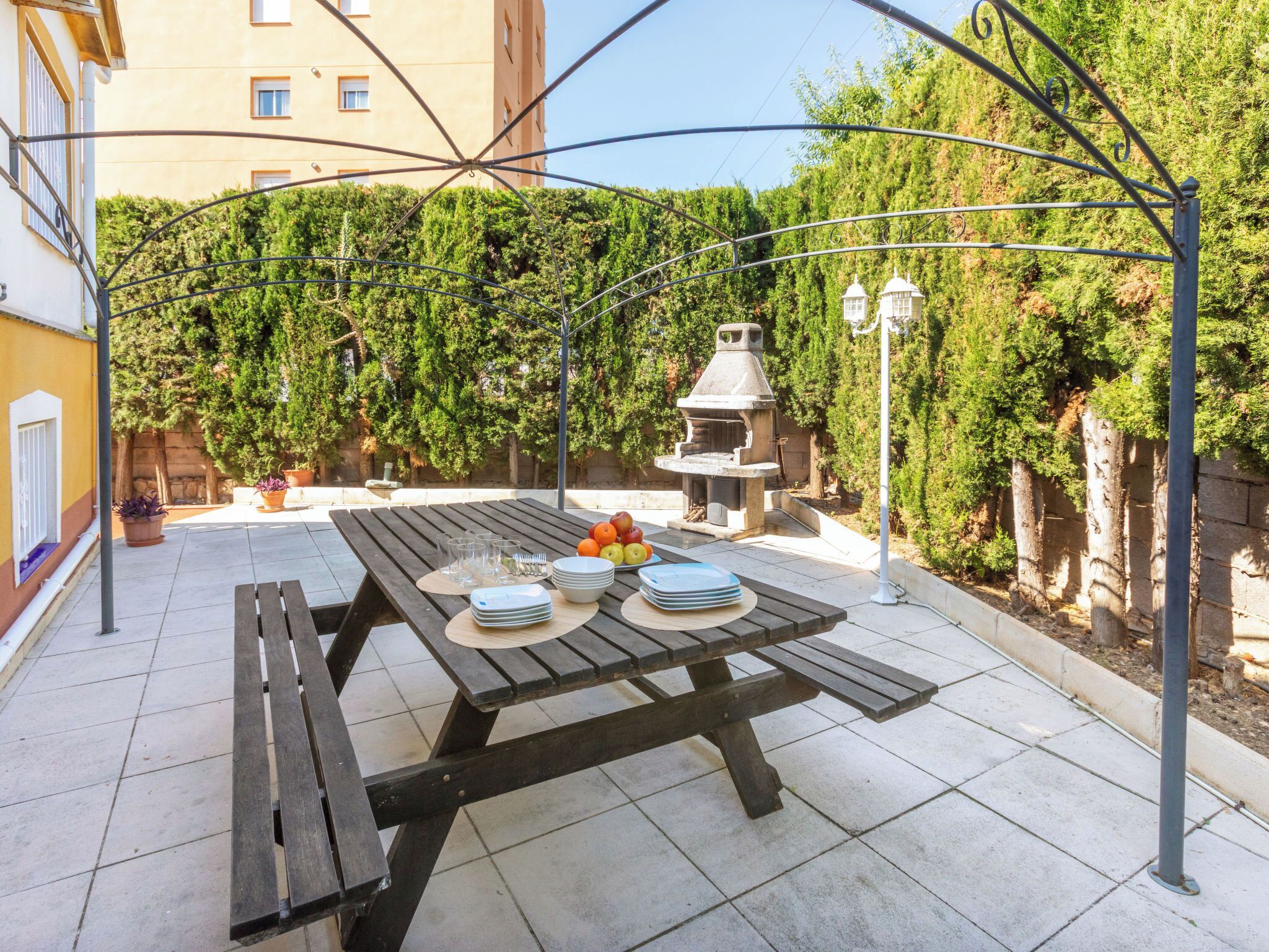 Een terras buiten met een houten eettafel, omgeven door een metalen pergola.