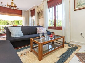 Ein Wohnzimmer mit einer Couch, einem Glastisch und Blick auf Grünfläche.