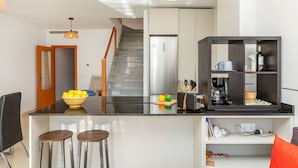 Une cuisine moderne dotée d’un îlot central, d’un coin repas avec une table et des chaises, et d’un escalier menant à un niveau supérieur.