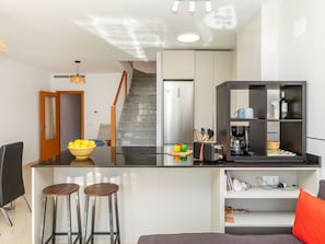 Eine moderne Küche mit einer zentralen Kochinsel, ein Essbereich mit Tisch und Stühlen sowie eine Treppe, die zu einer oberen Ebene führt.