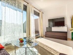 Ein modernes Wohnzimmer mit Glastisch, einer Couch, einem Flachbildfernseher und Blick ins Freie.