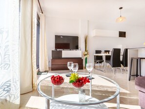 Ein modernes Wohnzimmer mit Glastisch, Fernseher und Essbereich.